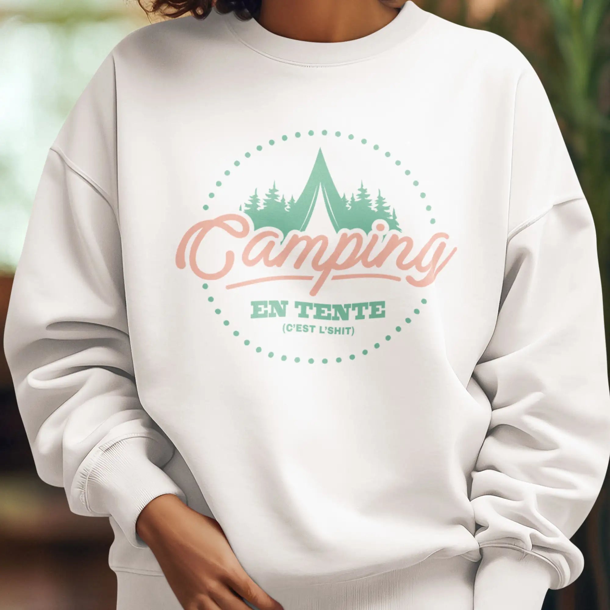 Sweatshirt en coton blanc avec un graphique circulaire prĂ©sentant des arbres verts, une tente, et le mot « camping » en script pĂȘche au-dessus de « en tente » en teal.