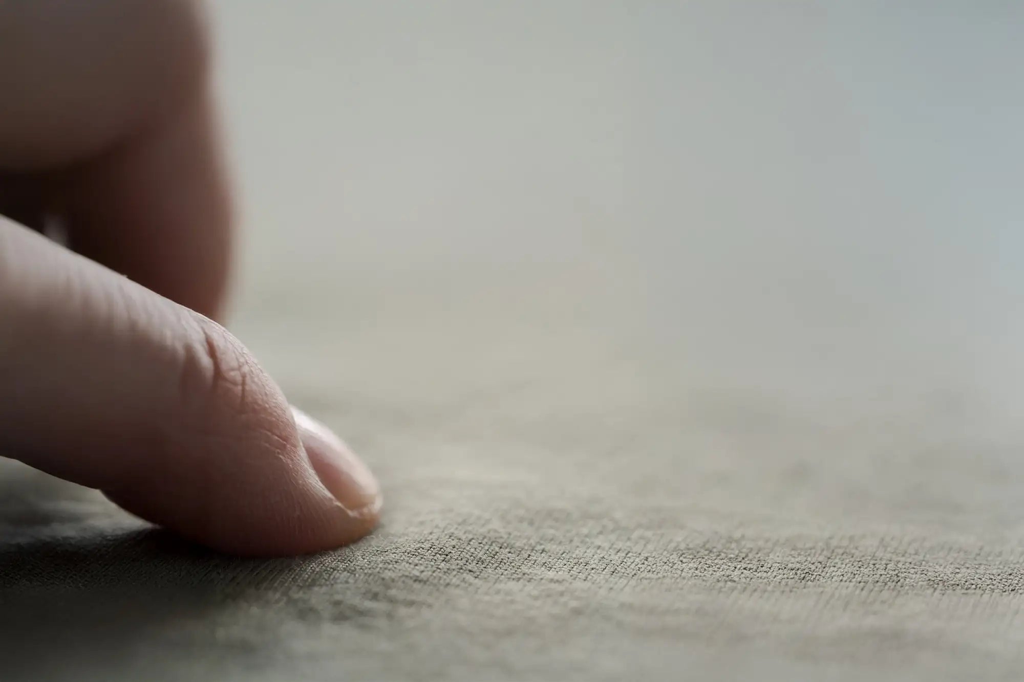 Un doigt repose doucement sur une surface de tissu texturé aux tons neutres.
