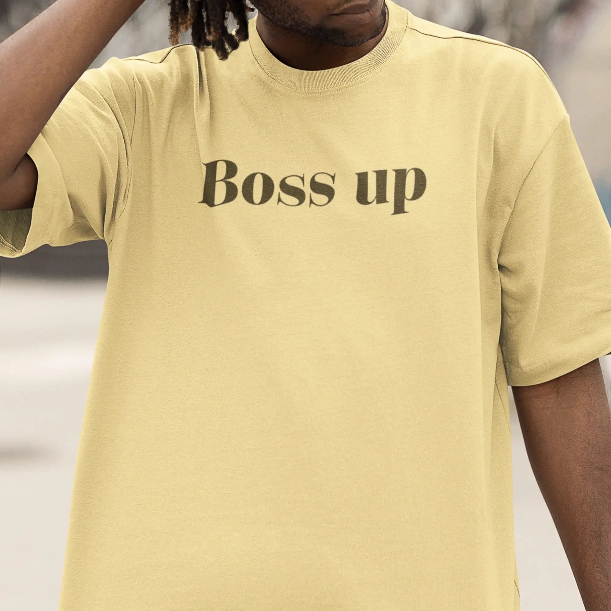 Un t-shirt ample à col rond de couleur jaune pâle avec « boss up » imprimé en police serif marron foncé sur la poitrine