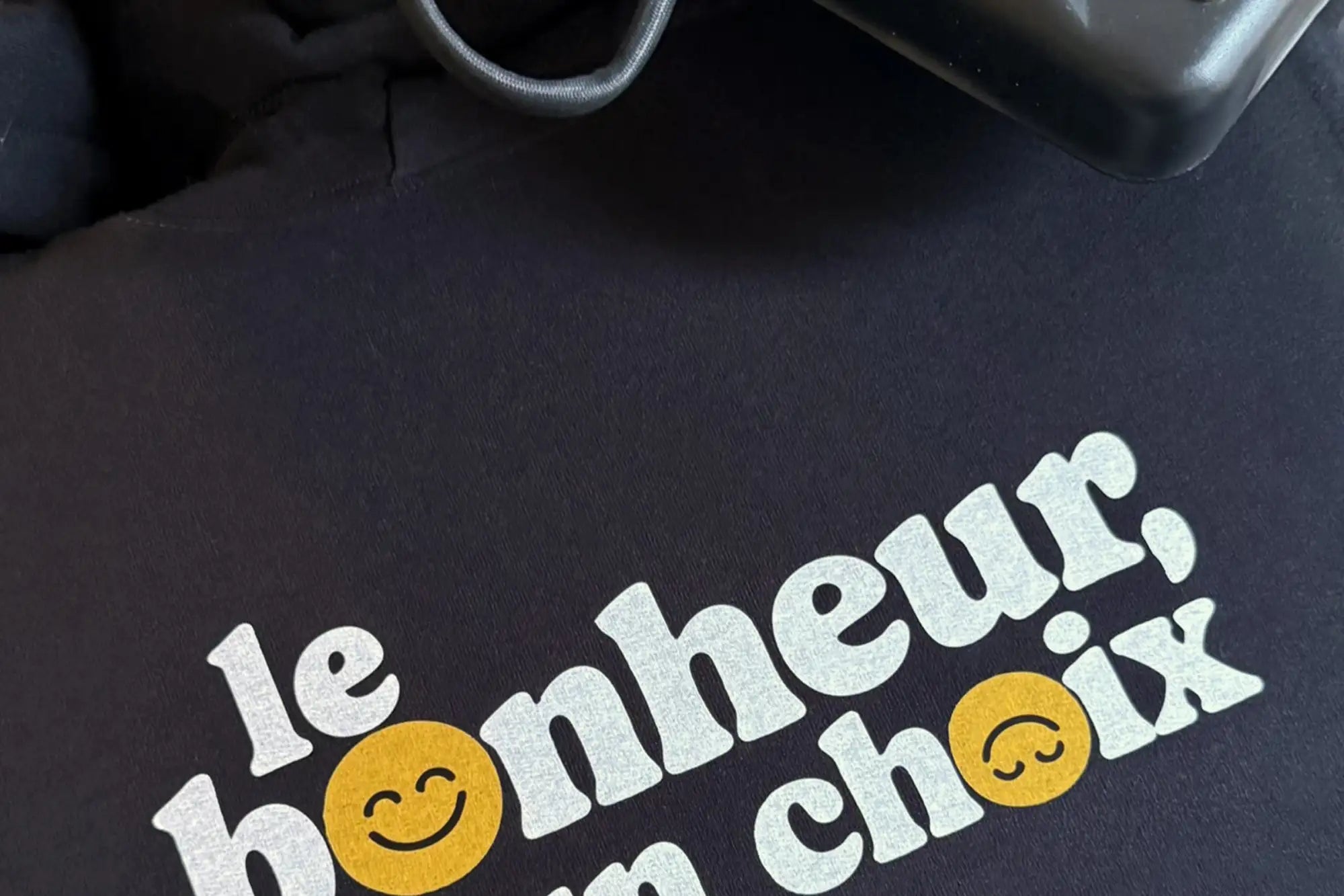 T-shirt noir avec graphique blanc et jaune indiquant 'le bonheur, un choix' orné de visages d'emojis souriants.